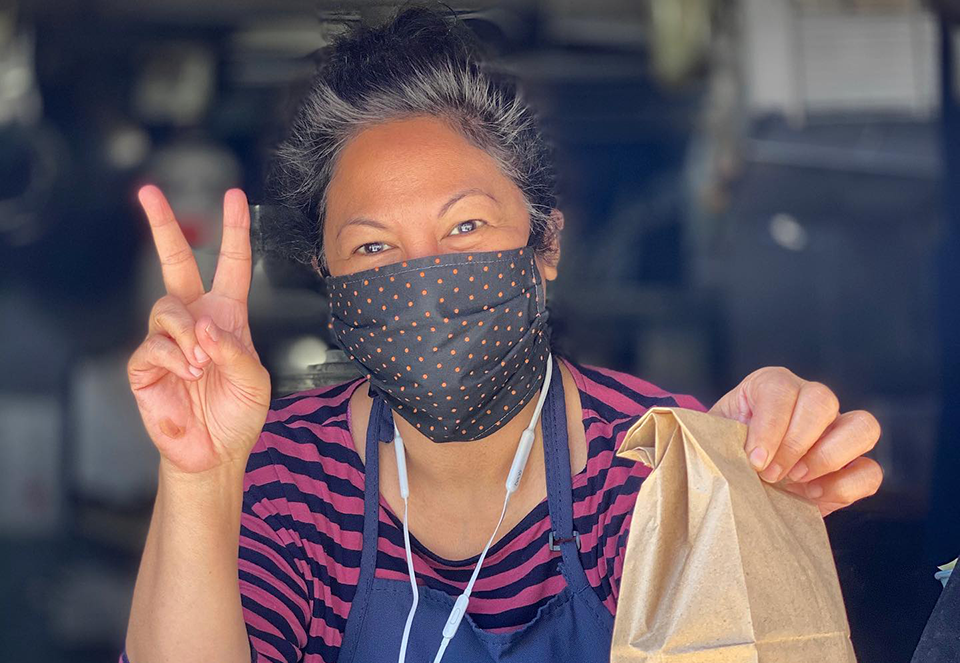 Knee High Stocking Co. co-owner Pamela Carpio with a mask on holding out an order.