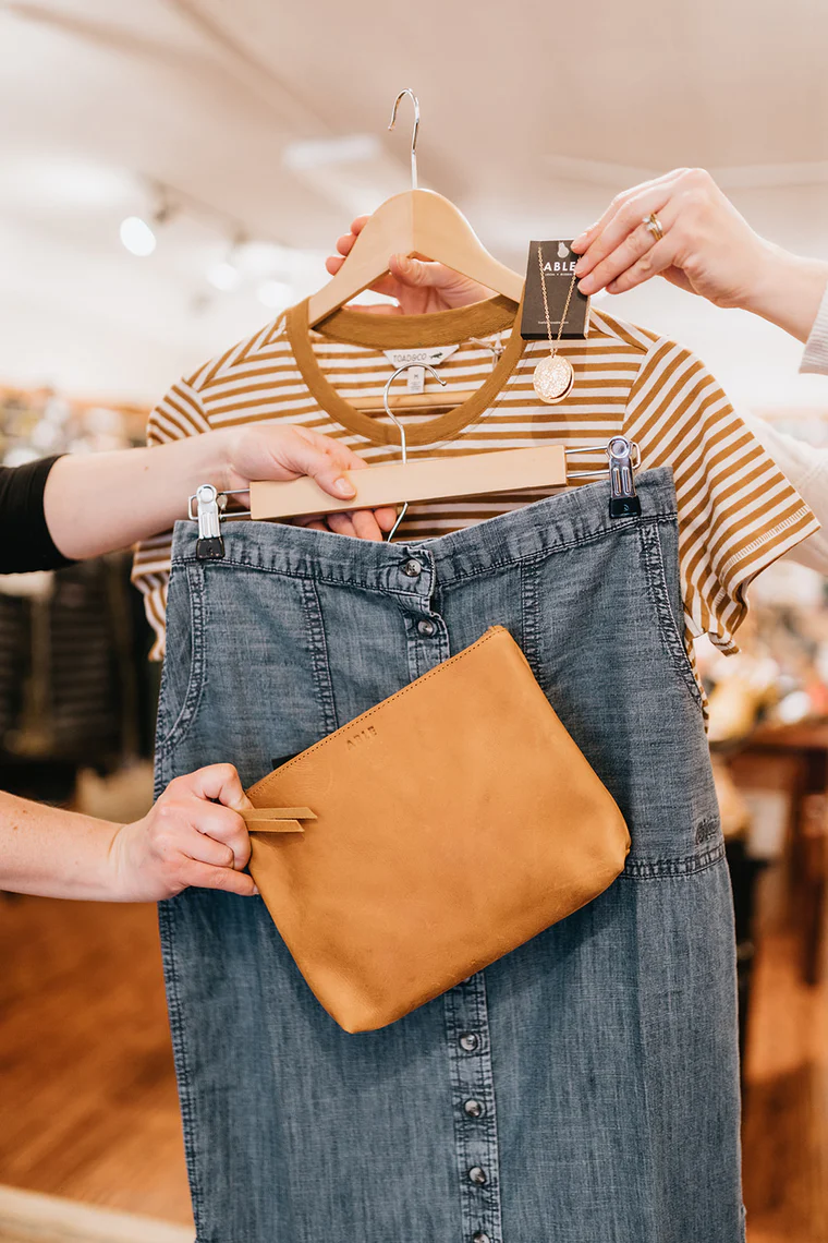 Hands holding up a t-shirt, jeans, clutch, and a necklace.