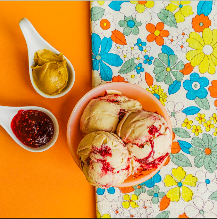 A bowl of ice cream with spoonfuls of nutbutter and jam on the side