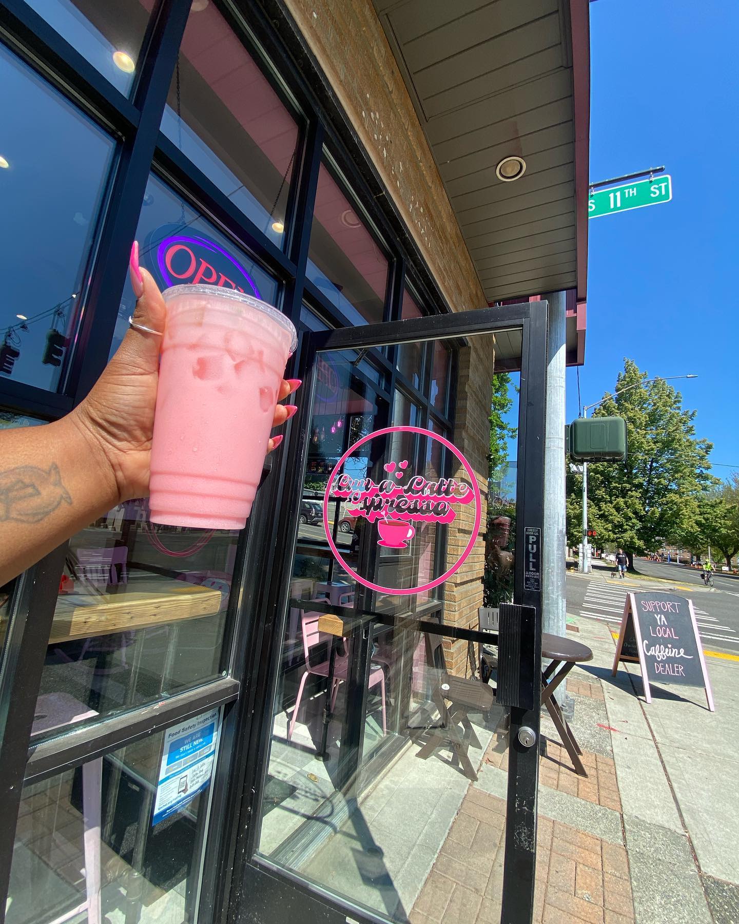 Luv-a-Latte owner's hand holding a pink drink out in front of the coffee shop front door