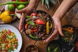 photo of a person holding out a bowl of ethiopian tibs with grilled red, green, and yellow bell peppers
